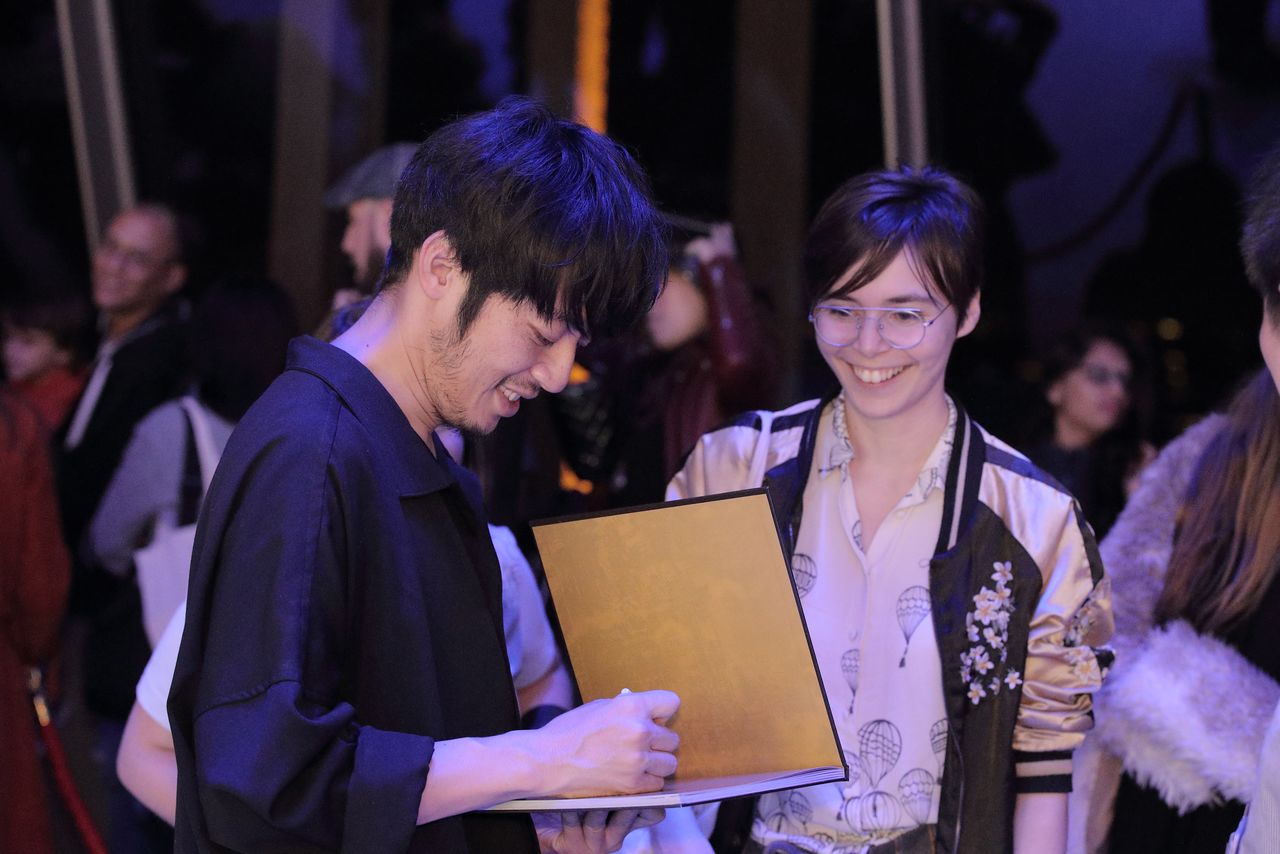 Nishino Akihiro en train de dédicacer un album sous les yeux d’une admiratrice éblouie, à l’occasion de l’exposition qui s’est tenue à la fin du mois d’octobre 2019 dans le Salon Gustave Eiffel de la tour Eiffel.