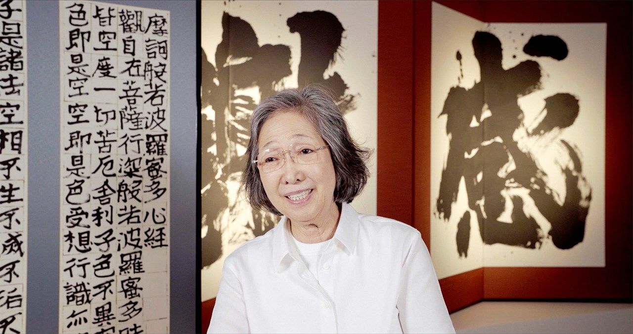 Kanazawa Yasuko est interviewée devant la calligraphie de Shôko intitulée « Sutra du cœur empreint de larmes » (à gauche sur la photo). (© Masterworks)