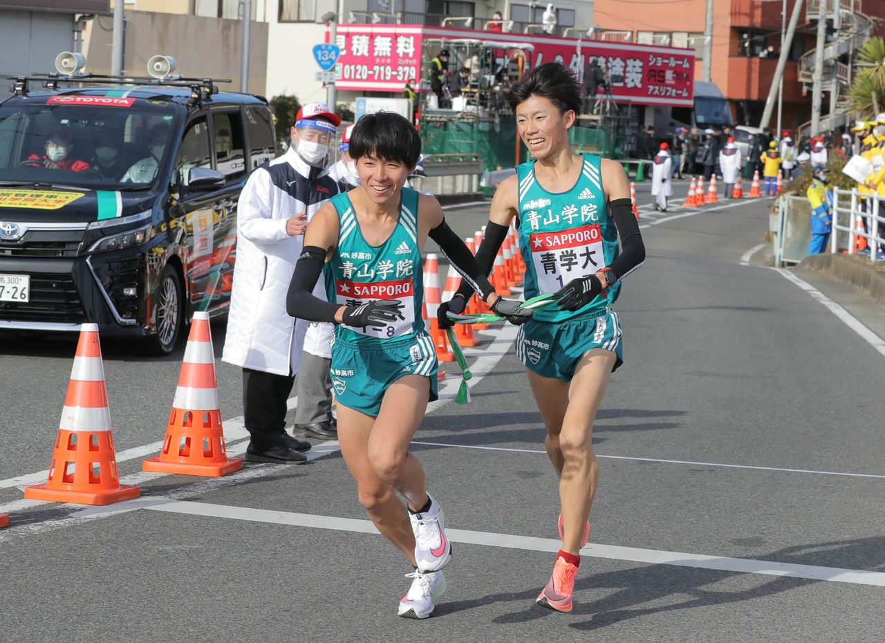 Kondô Kôtarô, de l'université Aoyama Gakuin, à droite, termine la septième étape du Hakone Ekiden 2021, remettant le tasuki à son coéquipier Iwami Shûya, coureur de la huitième étape. L'équipe avait terminé à la quatrième place cette fois-ci, mais elle a été redoutable ces dernières années, remportant six des huit courses effectuées depuis 2015. La photo a été prise au point de relais situé à Hiratsuka, dans la préfecture de Kanagawa, le 3 janvier 2021. (Jiji)