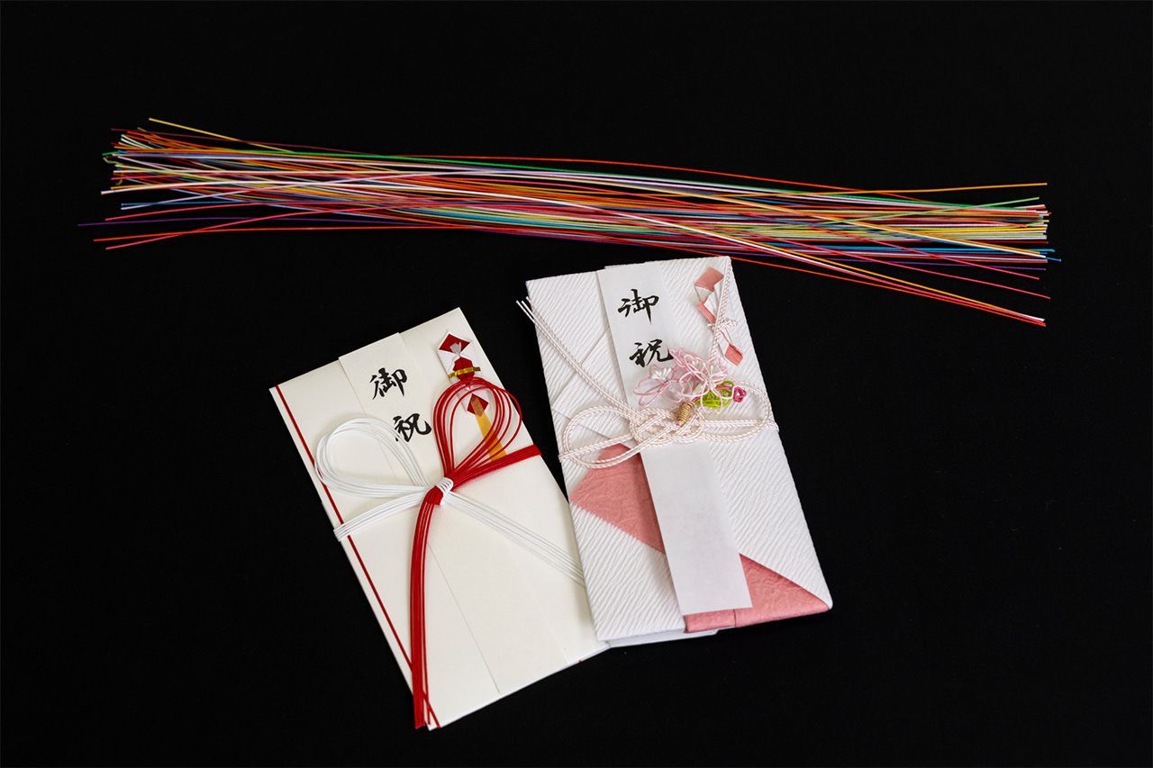 La plupart des Japonais connaissent bien l’utilisation de cordelettes mizuhiki pour décorer les enveloppes de dons d’argent (lors des mariages et des naissances entre autres). Le modèle le plus fréquent est celui de cordelettes blanches et rouges nouées en fleur, dans le style hana musubi (gauche). La variante imaginée par Morita Eriko (droite) utilise un nœud bien plus détaillé, appelé awabi-musubi (« nœud de l’ormeau »). (© Kawamoto Seiya)