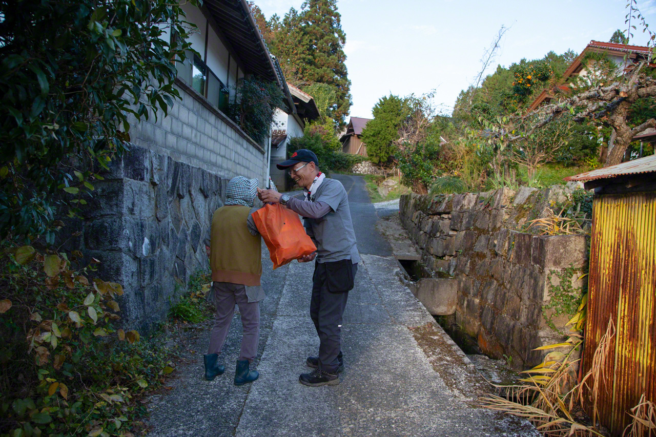 Takada aide une femme &agrave; porter son sac de courses jusqu'&agrave; chez elle.