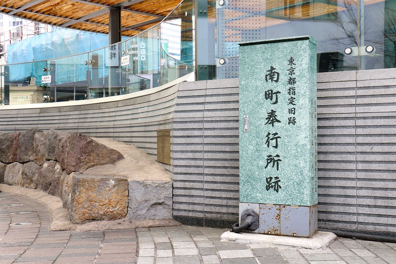 La stèle marquant l’emplacement de l’ancien poste de magistrature du Sud se dresse sur la place devant la gare JR de Yûrakuchô. Sur la gauche, on peut voir l’alignement de pierres qui bordait autrefois le caniveau, aujourd’hui exposé comme monument commémoratif. (Pixta)