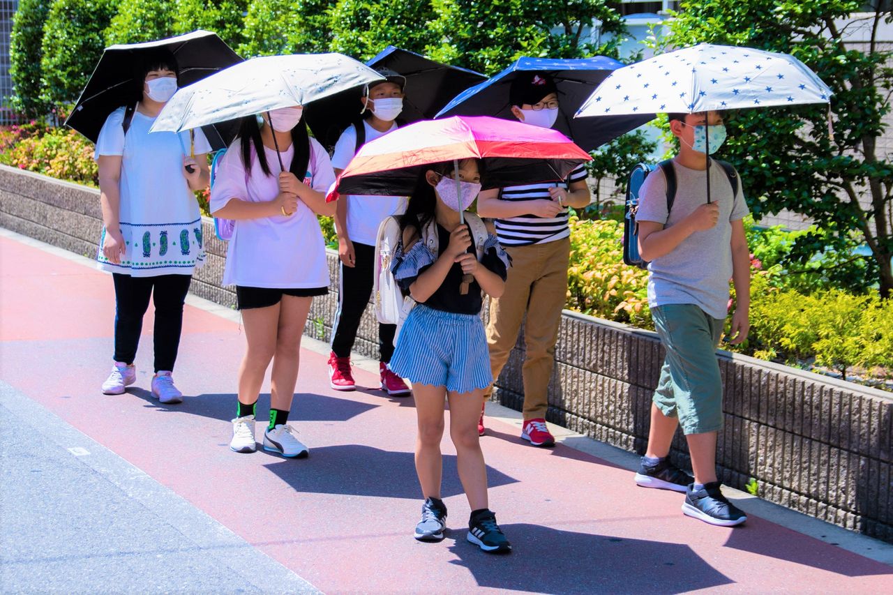 Des écoliers utilisant des ombrelles comme rempart contre la lumière et la chaleur. Les ombres projetées par les ombrelles sont bien visibles sur le trottoir (avec l'aimable autorisation de World Party).