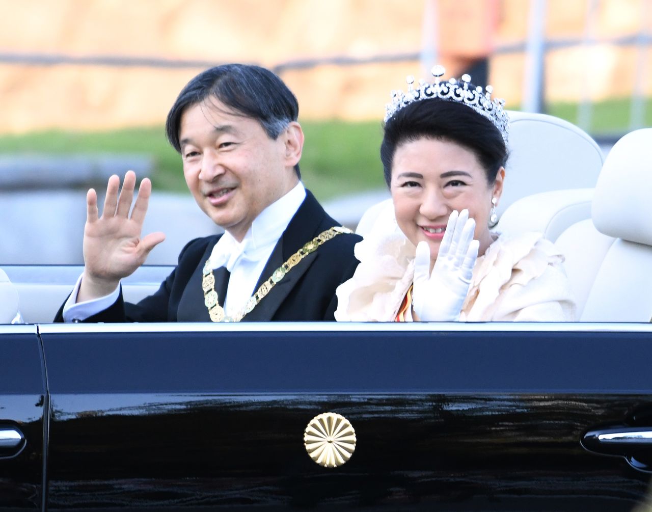 L’empereur Naruhito est vêtu d’un costume noir queue-de-pie et paré du collier de l’ordre suprême du chrysanthème. L’impératrice Masako est quant à elle habillée d’une longue robe blanche. Elle porte la tiare impériale et l’ordre de la couronne précieuse.