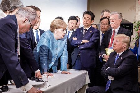 Juin 2018, à Charlevoix (Canada) : Abe Shinzô croisant les bras lors du G7, alors que la chancelière allemande Angela Merkel et le président Emmanuel Macron engagent une discussion musclée avec le président américain Donald Trump.
