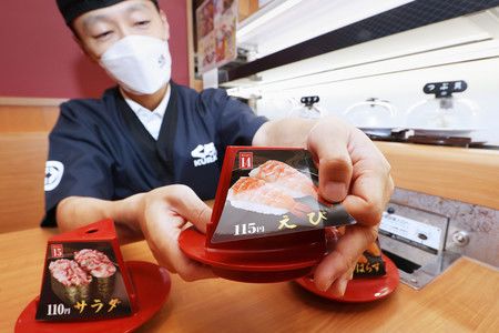 Un employé d'un restaurant de sushis sur tapis roulant change l'étiquette du prix.