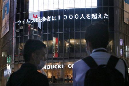 Un écran dans le quartier de Shibuya à Tokyo diffuse l’information disant que la barre des 1 000 cas au total en une journée a été dépassée le 29 juillet.