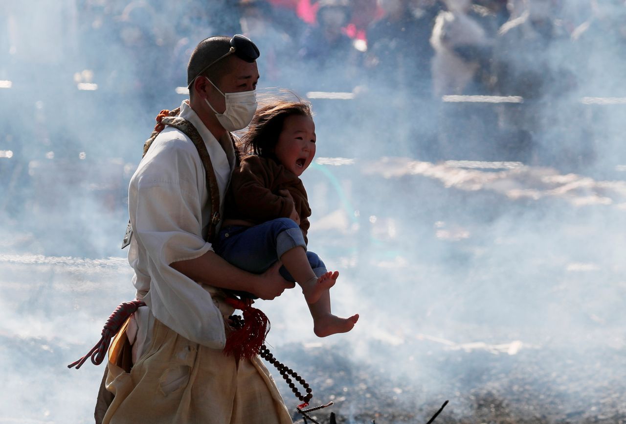 Un moine bouddhiste vêtu d’un masque de protection porte un enfant pendant la marche sur le feu du festival(le 14 mars 2021 au mont Takao. REUTERS/Kim Kyung-Hoon)