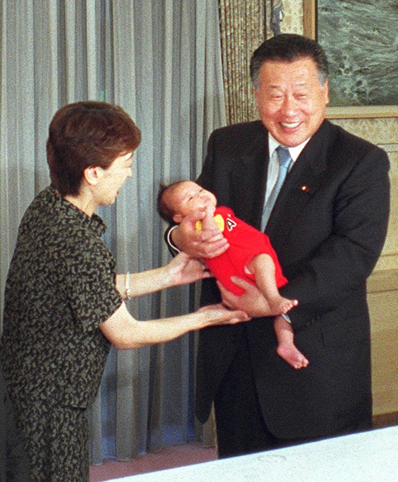 Le Premier ministre Mori Yoshirô porte la fille de Hashimoto, Seika, âgée d'un mois, en juin 2000. Hashimoto, qui a elle-même été nommée en l'honneur des Jeux olympiques de Tokyo de 1964, a choisi pour sa fille le nom de “Seika” (qui signifie « flamme olympique ») en hommage aux Jeux de Sydney de l’an 2000, année de sa naissance. (© Cabinet Office / Jiji) 