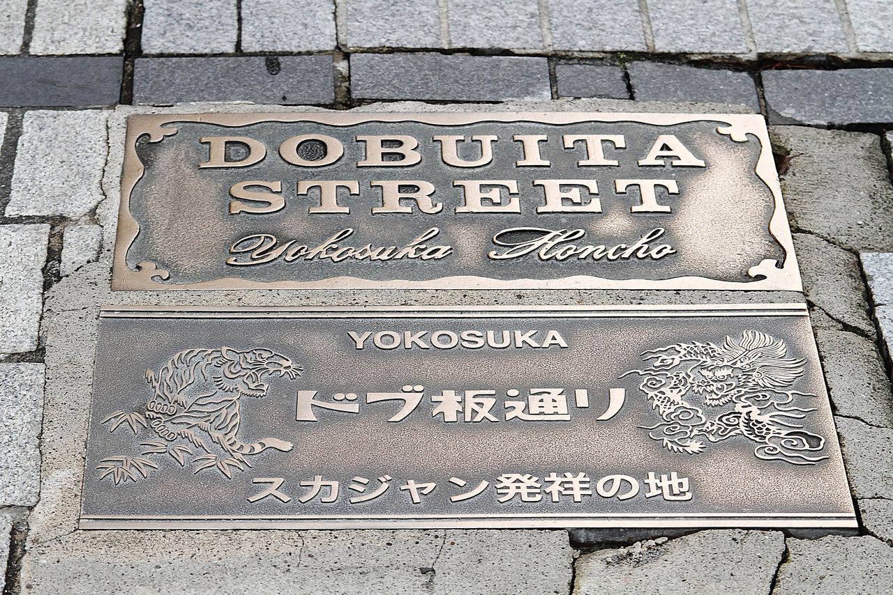 鑲嵌在Dobu板通商店街的金屬板，上面刻有「Sukajan發祥地」字樣