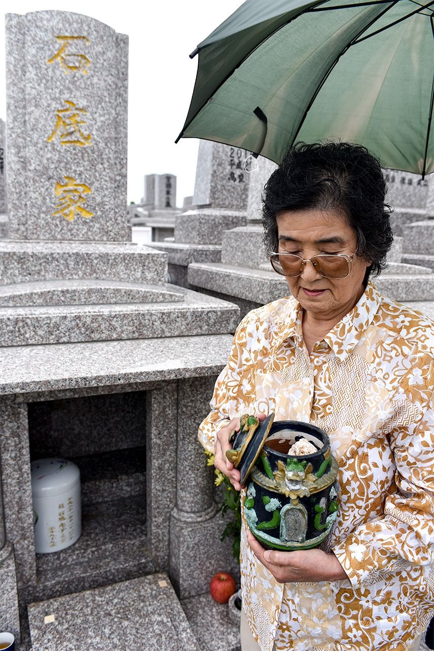 三女具志堅美智惠在石底加彌墓前抱著骨灰罈，照片裡可以看見罈中石頭，2019年5月28日，沖繩縣糸滿市（筆者攝影）
