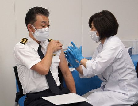 接受新型冠狀病毒疫苗施打的全日本空輸機師（左）＝13日上午、東京都大田區羽田機場
