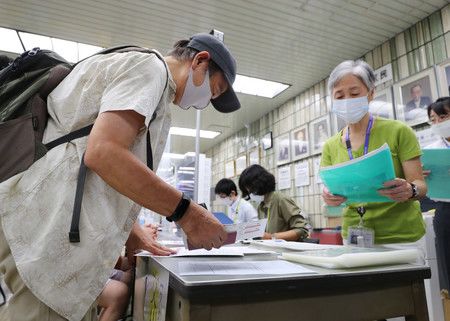 領取新型冠狀病毒疫苗施打證明「疫苗護照」的人（左）＝26日上午、東京都品川區