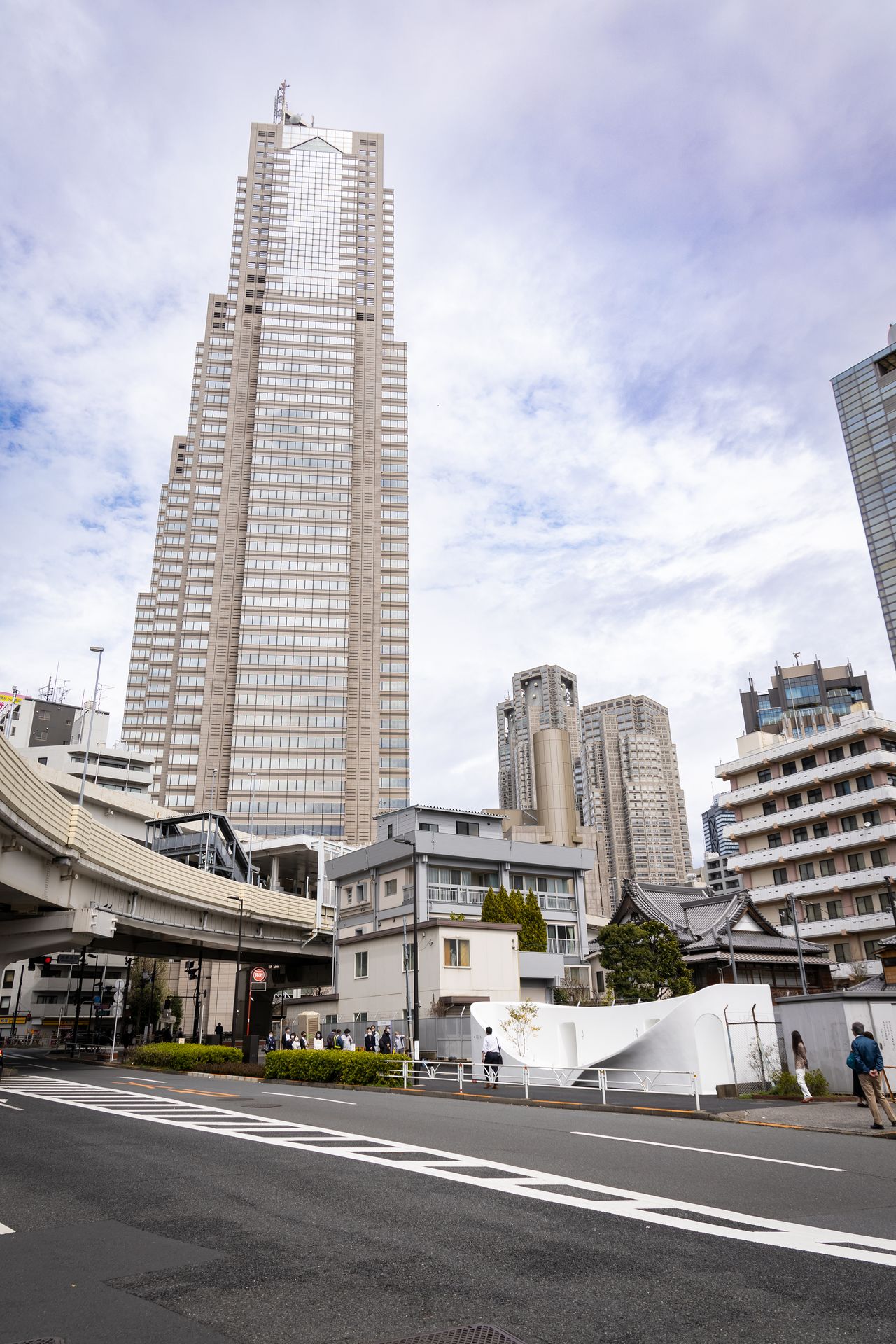 都会の中で浮き立つような真っ白な公衆トイレ。背後にはパークハイアット東京や都庁の高層ビルが見える