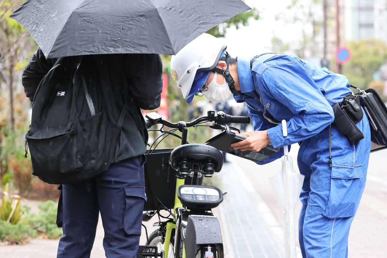 傘差し運転を取り締まる警察官=2026年4月1日・岡山市(山陽新聞/共同)