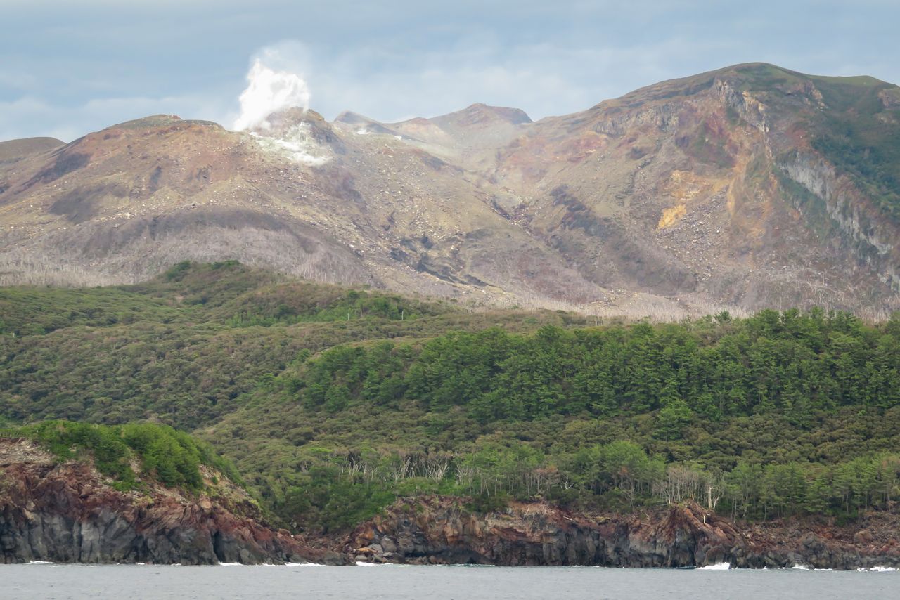 海上から浸食崖の向こうに、煙を上げる新岳と古岳（右）を望む　写真：PIXTA