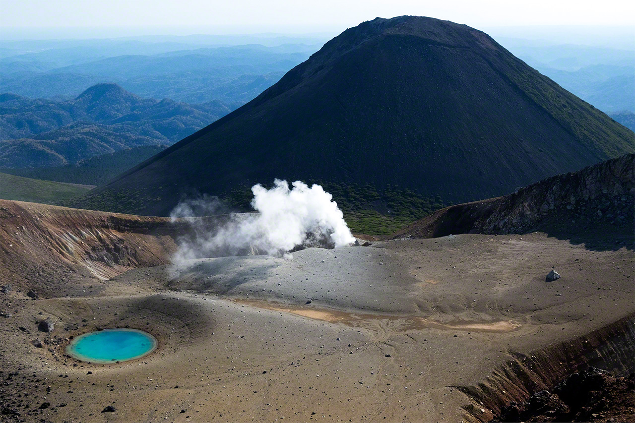 火山活動が見られる雌阿寒岳の青沼と背後にそびえる阿寒富士（1476メートル、）