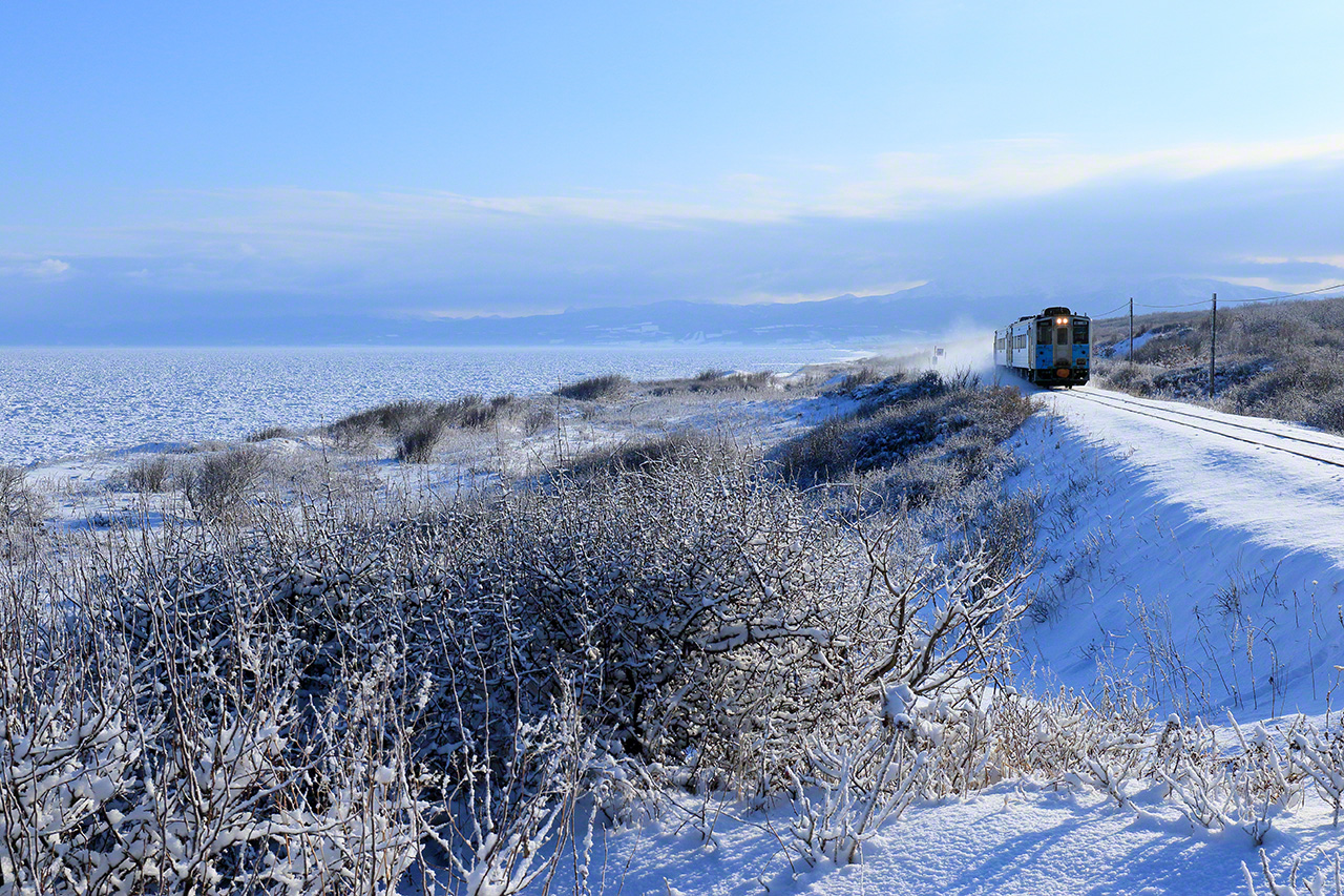JR釧路本線の止別〜知床斜里間（北海道斜里町）を走るキハ54形気動車。2月。オホーツク海の流氷が接岸したのを確認して、撮影に向かった。左側に見えるのは流氷だが、接岸すると雪原と見分けがつかなくなる。
