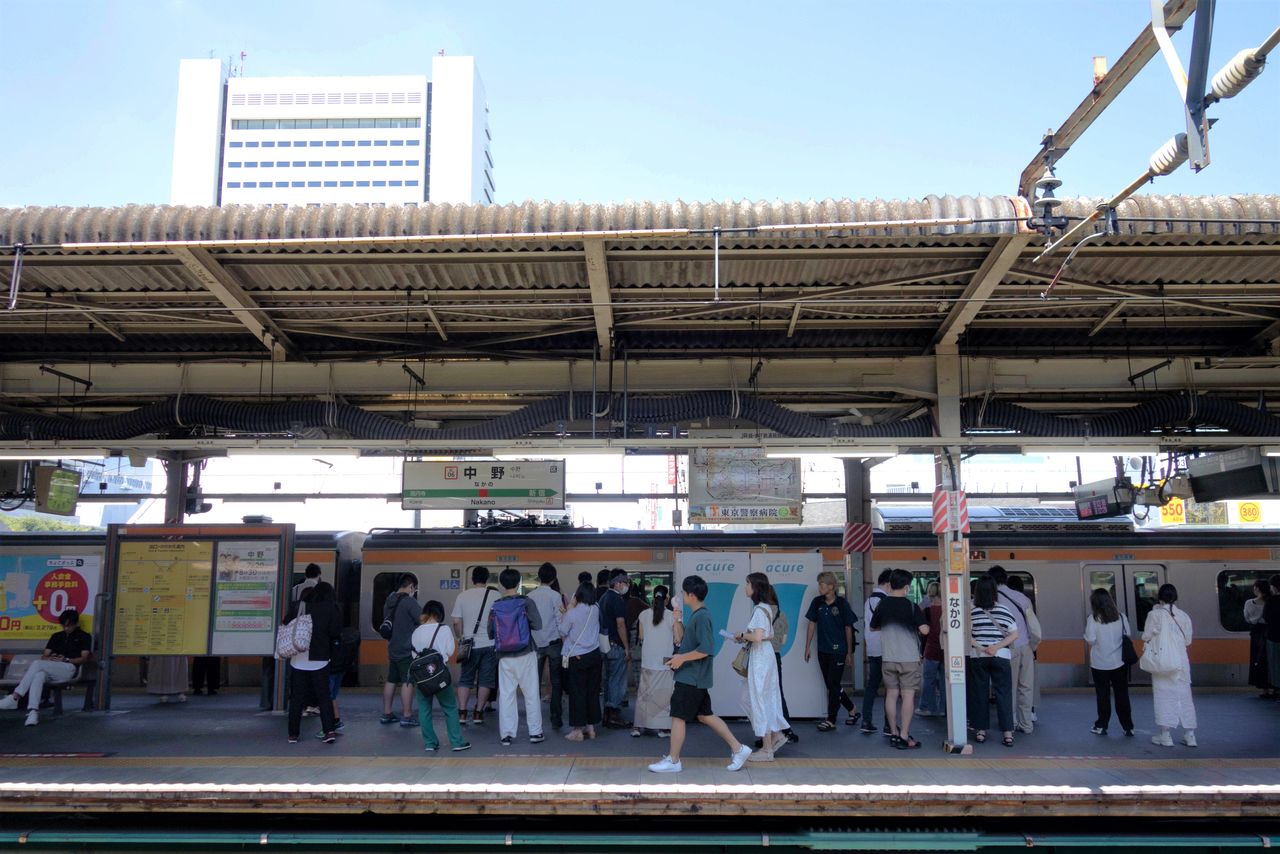 中野駅に停車中の中央線の電車。オレンジ色のラインが象徴的だ。背後に見えるのは7月2日に閉館した中野サンプラザ。今後の解体、再開発が決まっている　写真＝フクサコアヤコ