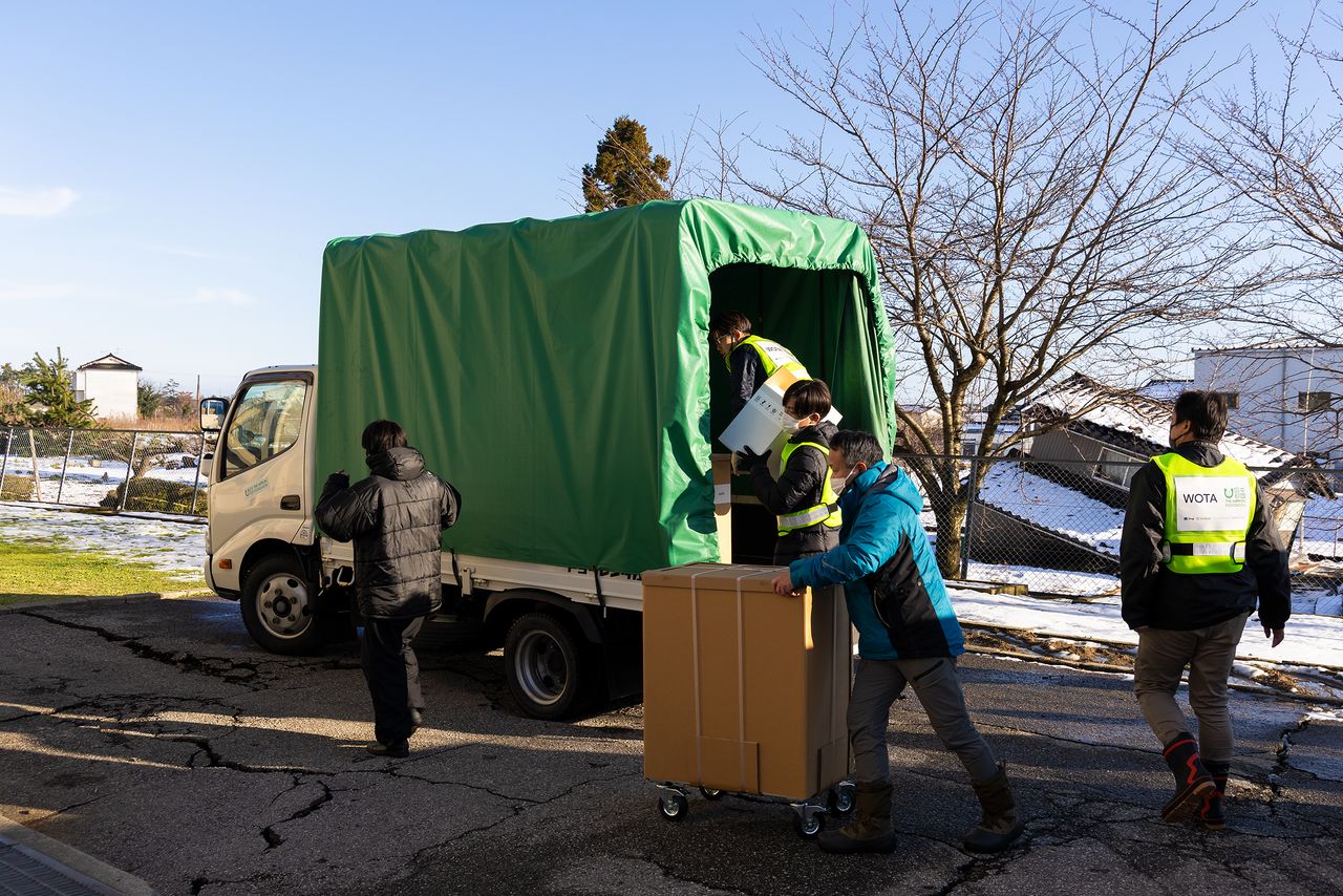 校舎裏でトラックからの荷降ろし作業。目の前にも、倒壊した建物が