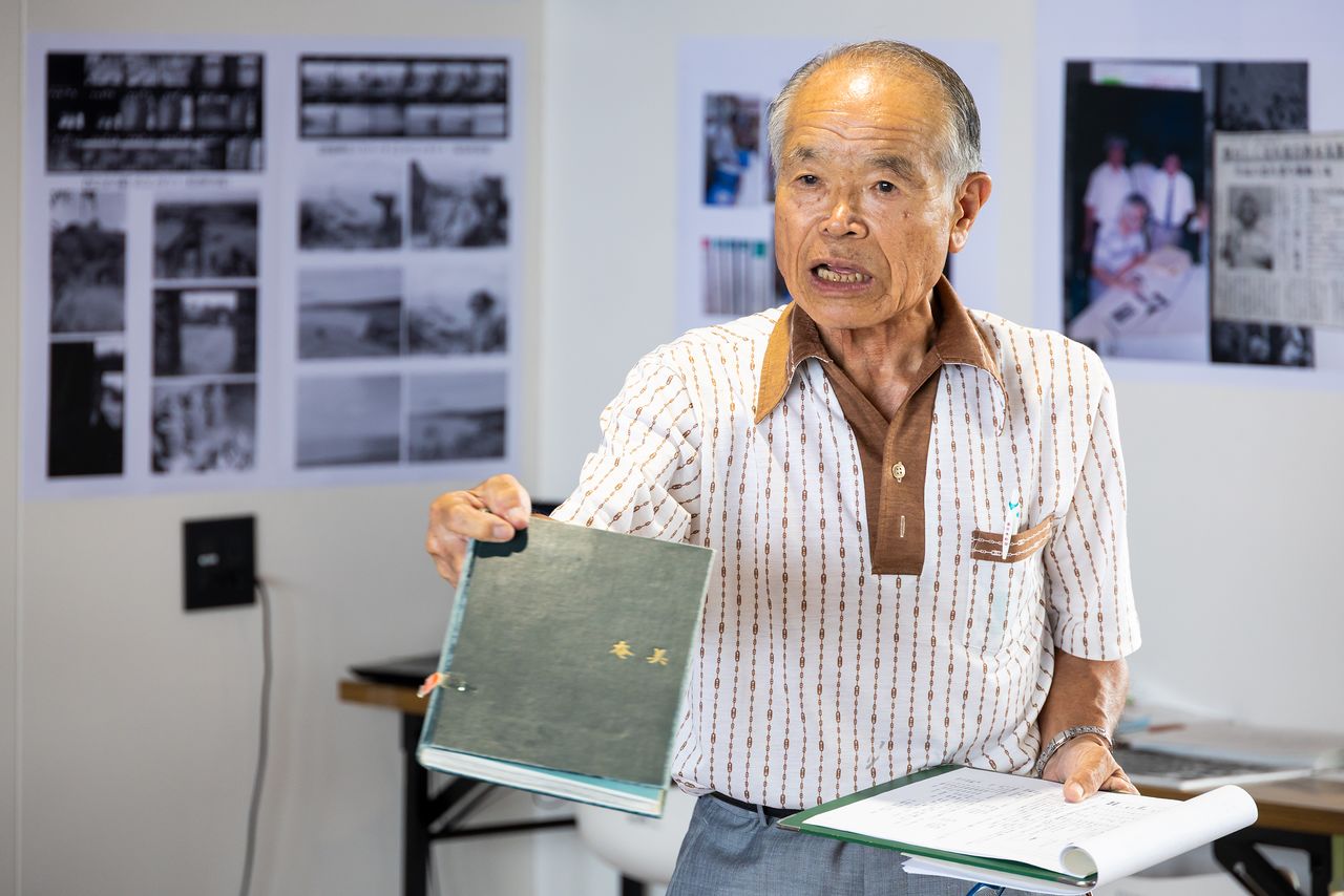 『奄美』を参考に寄贈写真を解説する先田さん(ニッポンドットコム撮影)