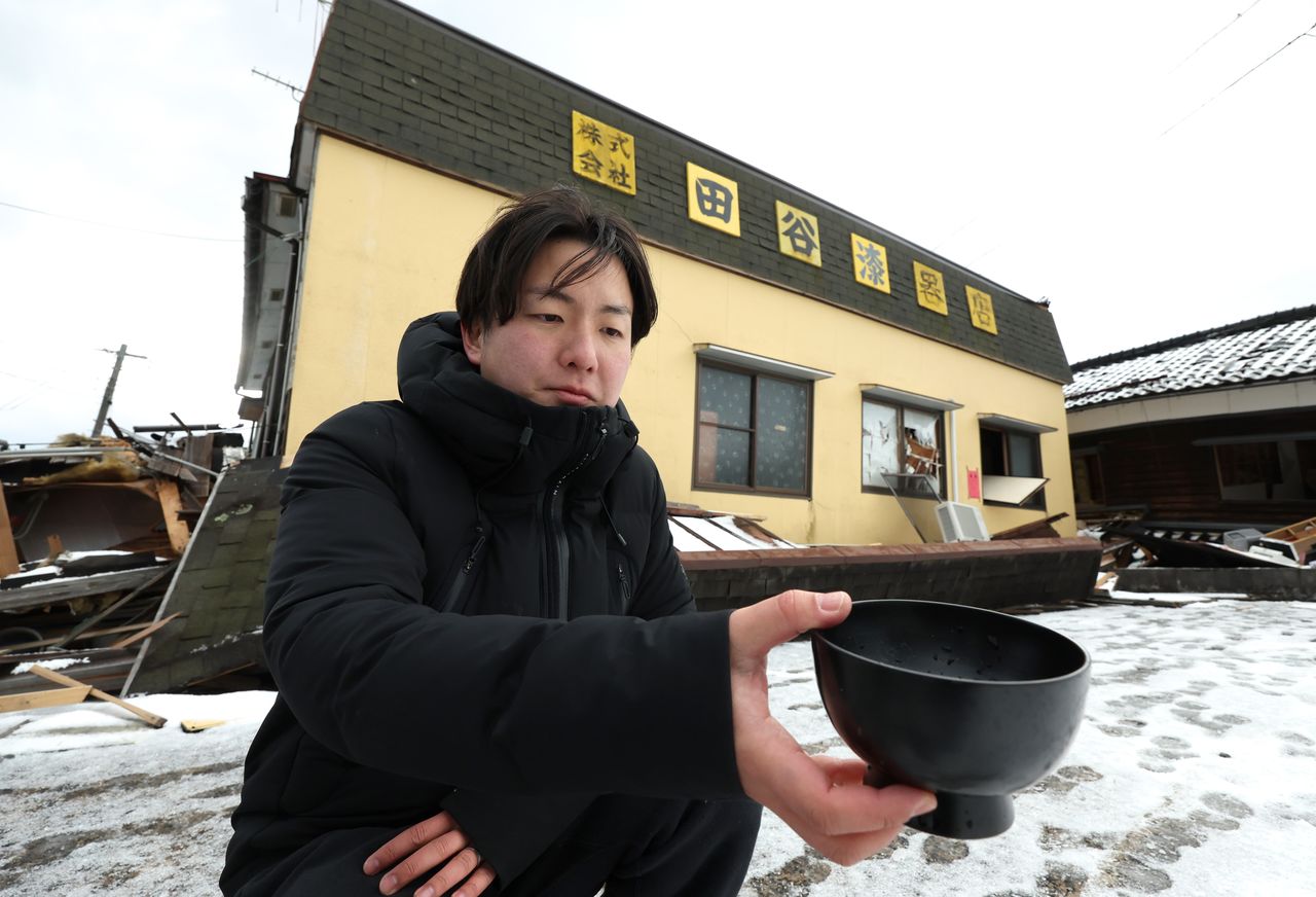 1階部分が押しつぶされた工房から見つかった輪島塗の漆器を持つ田谷昂大代表=2024年1月16日、石川県輪島市(時事)
