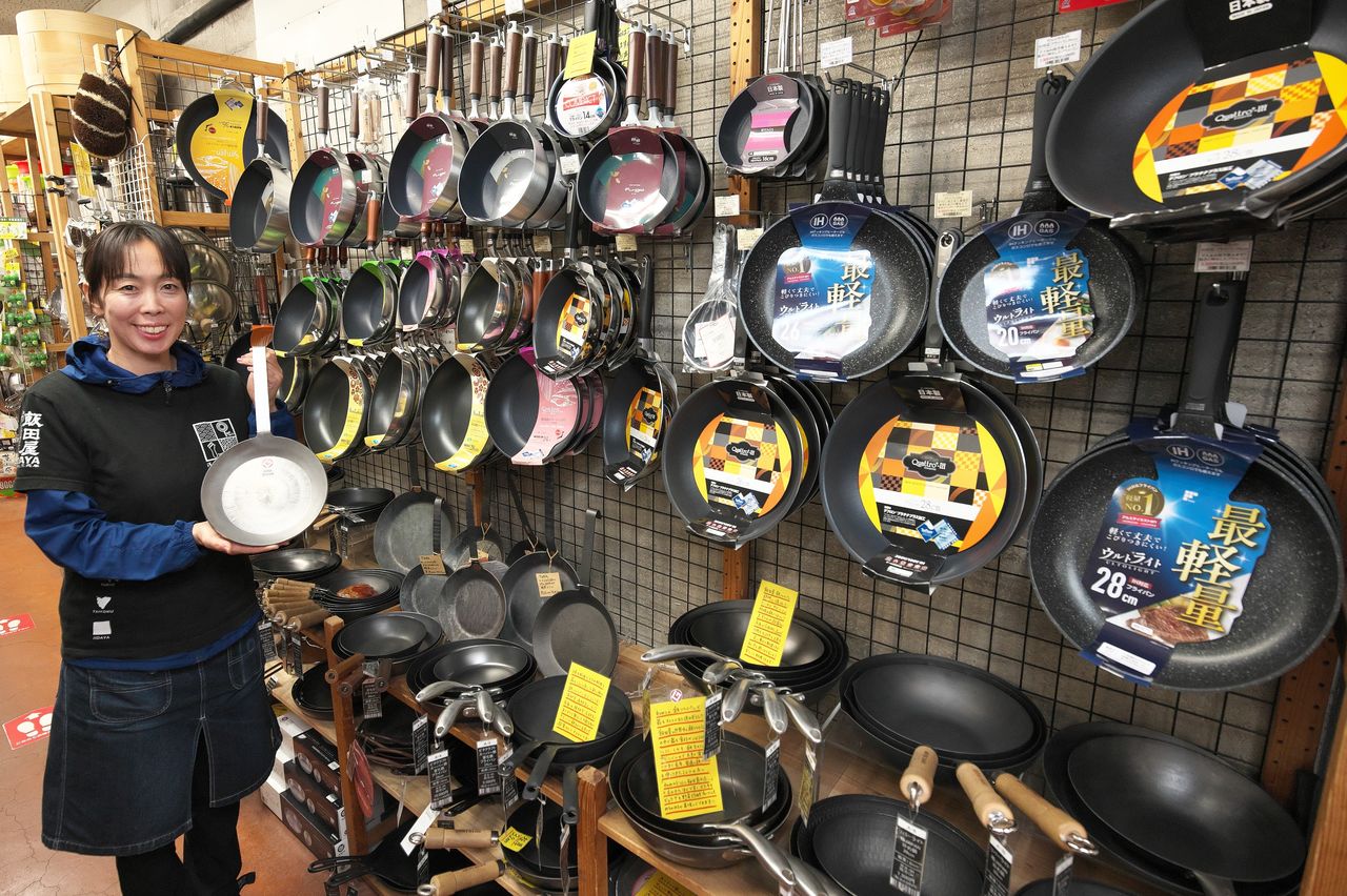 ステンレス製のエバーグリルを手にするスタッフ。売り場にはさまざまなフライパンが並ぶ