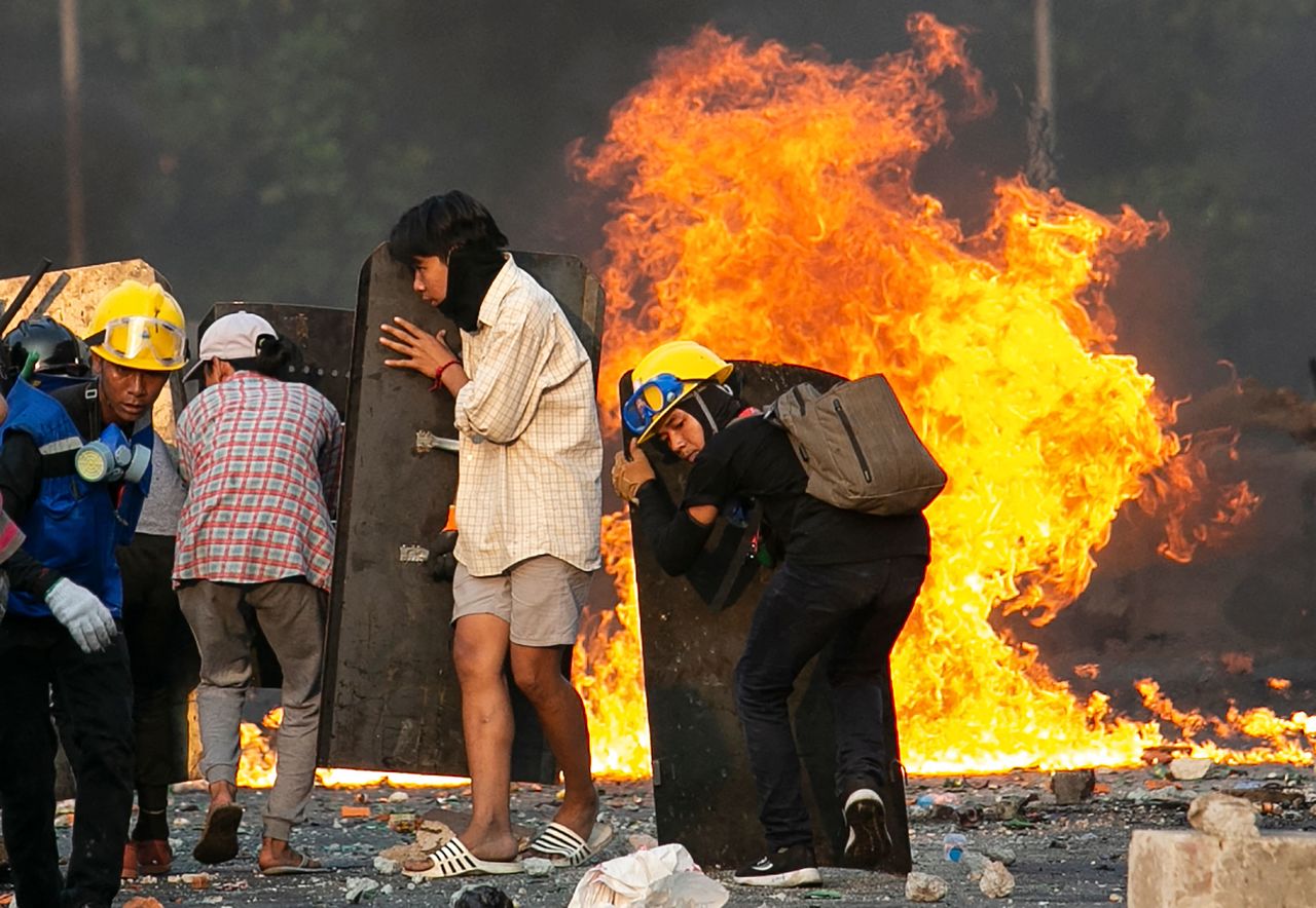 ヤンゴンの通りで、炎をよけるミャンマーのデモ隊（ミャンマー・ヤンゴン）2021年03月16日　AFP＝時事
