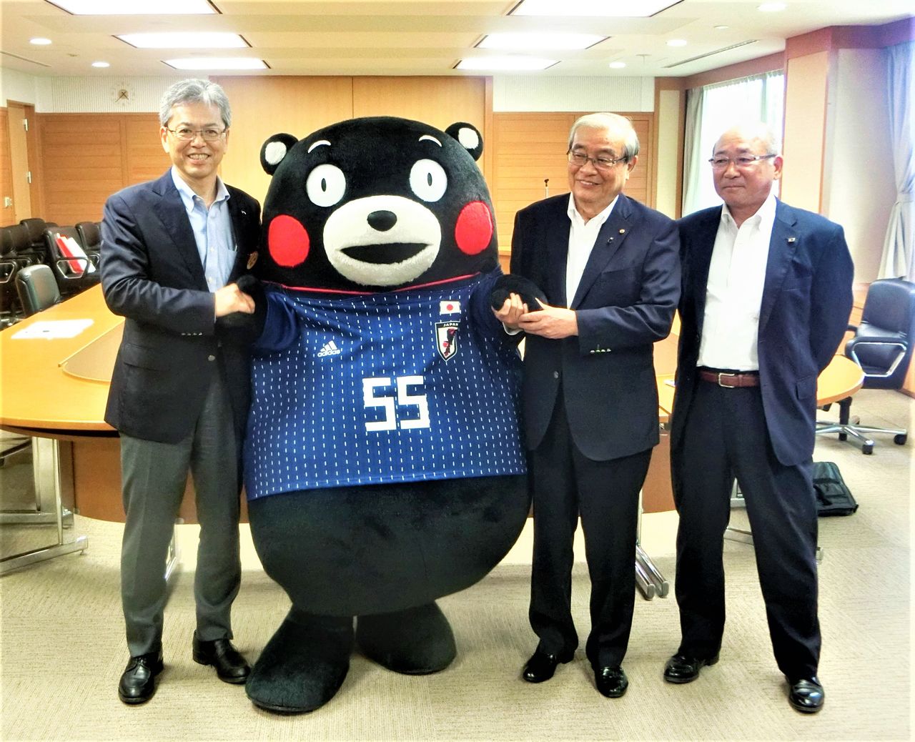 贈呈された日本代表のユニホームを着たくまモンと、熊本県サッカー協会関係者ら(2018年5月17日、熊本市・熊本県庁) 時事