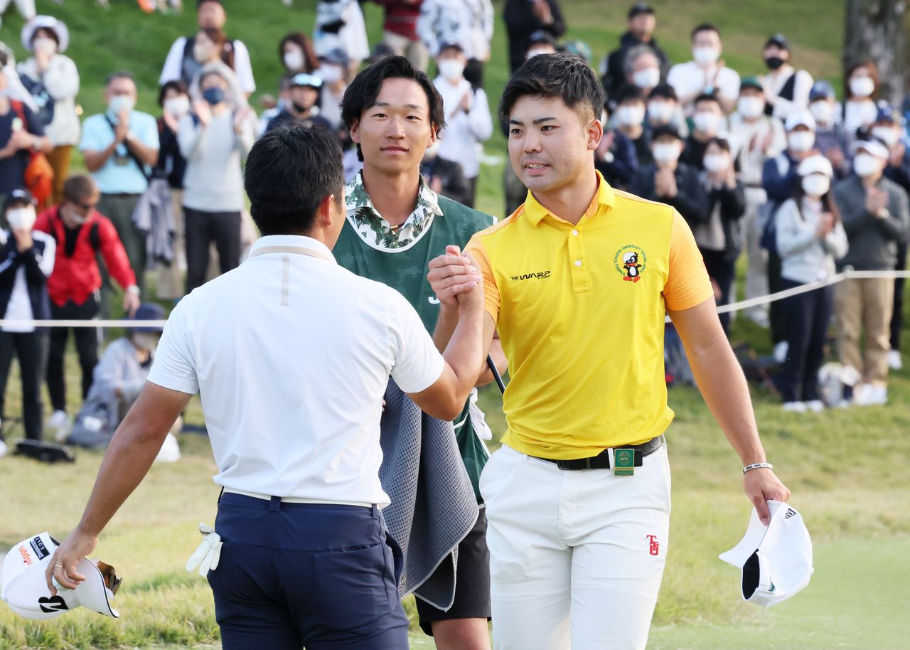 日本オープンゴルフ最終日、18番をホールアウトし、2位の比嘉一貴(左)と健闘をたたえ合うアマチュアの蝉川泰果(右)=2022年10月23日、兵庫・三甲GCジャパン(時事)