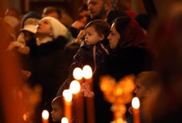 ことし1月7日、正教のクリスマスを迎えた首都キーウの修道院でろうそくをともして祈りをささげる親子（共同）