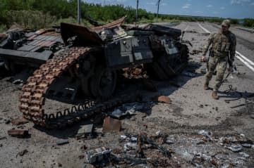 ウクライナ南部ザポロジエ州ロボティネ近くで破壊された戦車の横を歩くウクライナ兵＝25日（ロイター＝共同）