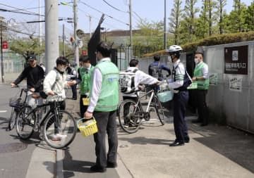 自転車通学の学生たちにヘルメットの着用を呼びかける警視庁成城署員ら＝4月、東京都世田谷区