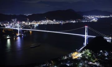 開通50周年を前にライトアップされた、北九州市（奥）と山口県下関市を結ぶ関門橋＝12日夜