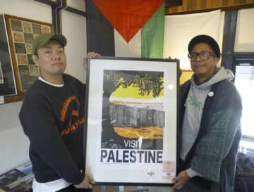 「VISIT　PALESTINE」と書かれたポスターを手にするアンディカ・ファイサルさん（右）＝14日、大阪市西区の「モモブックス」