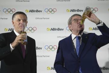 記者発表の席でアンハイザー・ブッシュ・インベブ社の飲料を口にするIOCのバッハ会長（右）と、同社のドゥケリスCEO＝12日、ロンドン（AP＝共同）
