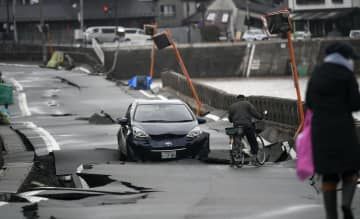 地震で波打った道路に残された車＝15日午前、石川県輪島市