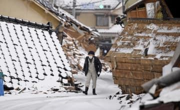雪が積もる石川県輪島市で、倒壊した家屋の前を歩く男性＝16日午前