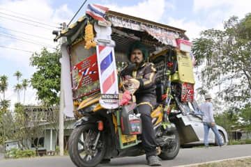 用具を積み込んだバイクにまたがる美容師のタナワットさん＝2023年12月、タイ・ブリラム郊外（共同）