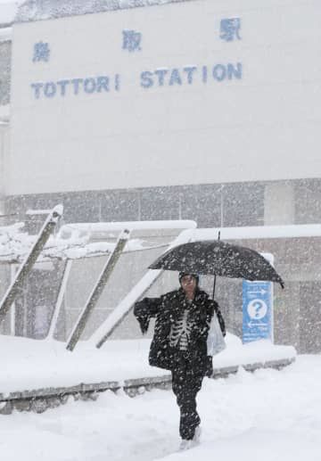 雪が降る中、JR鳥取駅前を歩く人＝24日午後