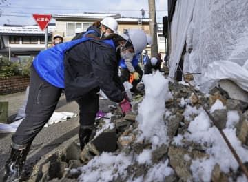 石川県七尾市のしょうゆ店で、雪に埋もれた外壁の破片を片付けるボランティア＝27日午後