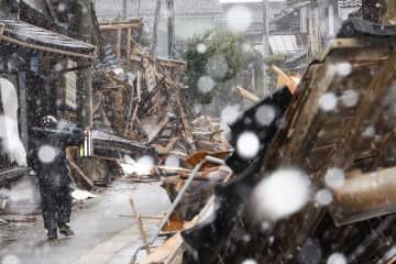 雪が降る石川県珠洲市内。道具を担いだボランティアが足早に歩いていた＝1日午後