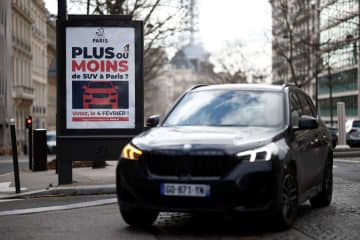 「SUVが必要かどうか」を問うポスターの前を走行する車＝2日、パリ（ロイター＝共同）