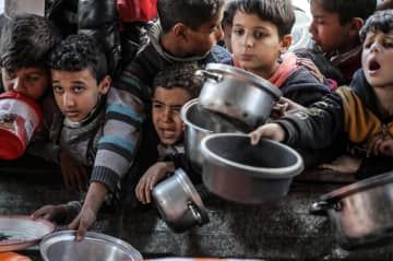 5日、パレスチナ自治区ガザのラファで、食料を求め鍋を差し出す子どもたち（ゲッティ＝共同）