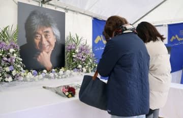 小澤征爾さんの笑顔の写真が飾られた献花台を訪れ、別れを惜しむ人たち＝10日午後、長野県松本市