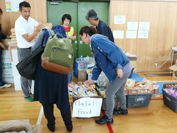 箕面市某所小学为大阪北部地震的避难所,外国人占多数。市政府工作人员正在对清真食品进行说明(2018年6月20日,时事社)