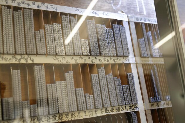 頻出単語をあらかじめ揃えた連字のケース。写真の活字棚は2003年まで使われていたもので、2002年までサッカー日本代表の監督だった「トルシエ」や、同年に引退したボクシングの世界王者「畑山（隆則）」などが並んでいる