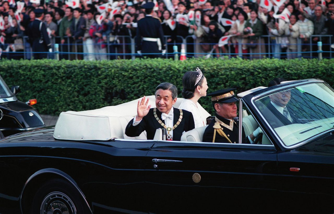 Император Акихито приветствует людей на проспекте Аояма в Токио во время проезда кортежа после церемонии восшествия на престол 12 ноября 1990 года (Jiji Press)