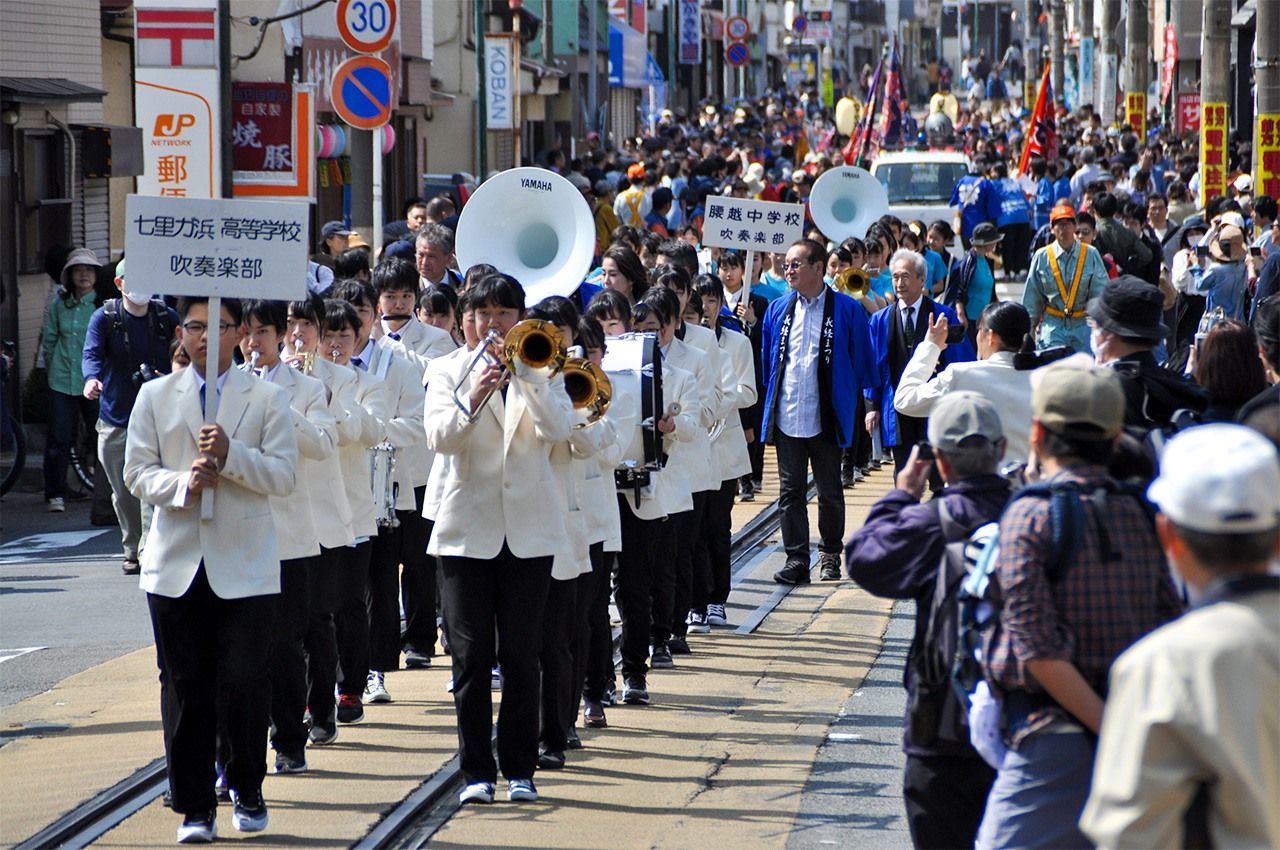 Духовой оркестр младших и старших классов местных школ проходит парадом вдоль железнодорожных путей Энодэн, его выступления пользуются успехом (предоставлено храмом Мампукудзи)
