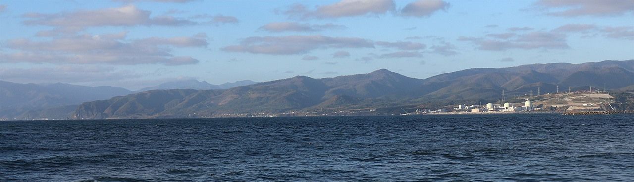 АЭС «Томари» (справа на переднем плане) и виднеющееся вдали (16 километрах дальше по полуострову Сякотан) село Камоэнай (© Мацумото Соити)